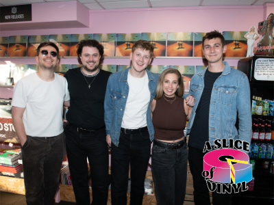THE COVASETTES standing together in a record store with a pink wall and shelves displaying records.